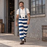 Biker barbu marchant devant un atelier en pantalon Folsom Prison rayé bleu et blanc, bretelles 1937 Heavy Duty de 45 mm et revers Hold Fast