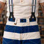 Gros plan des attaches en cuir noir des bretelles 1937 Heavy Duty de 45 mm Blue fixées aux boutons avant du pantalon bagnard bleu et blanc