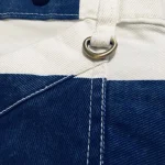 Gros plan du denim bleu, de l’anneau en laiton et des boutons pour bretelles